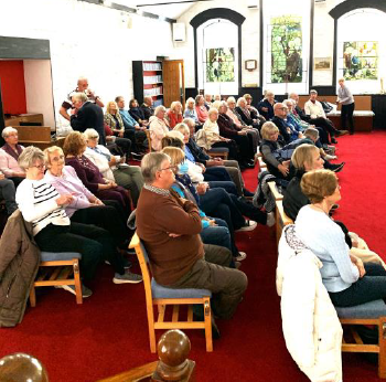 Members seated at a monthly meeting listening to a speaker